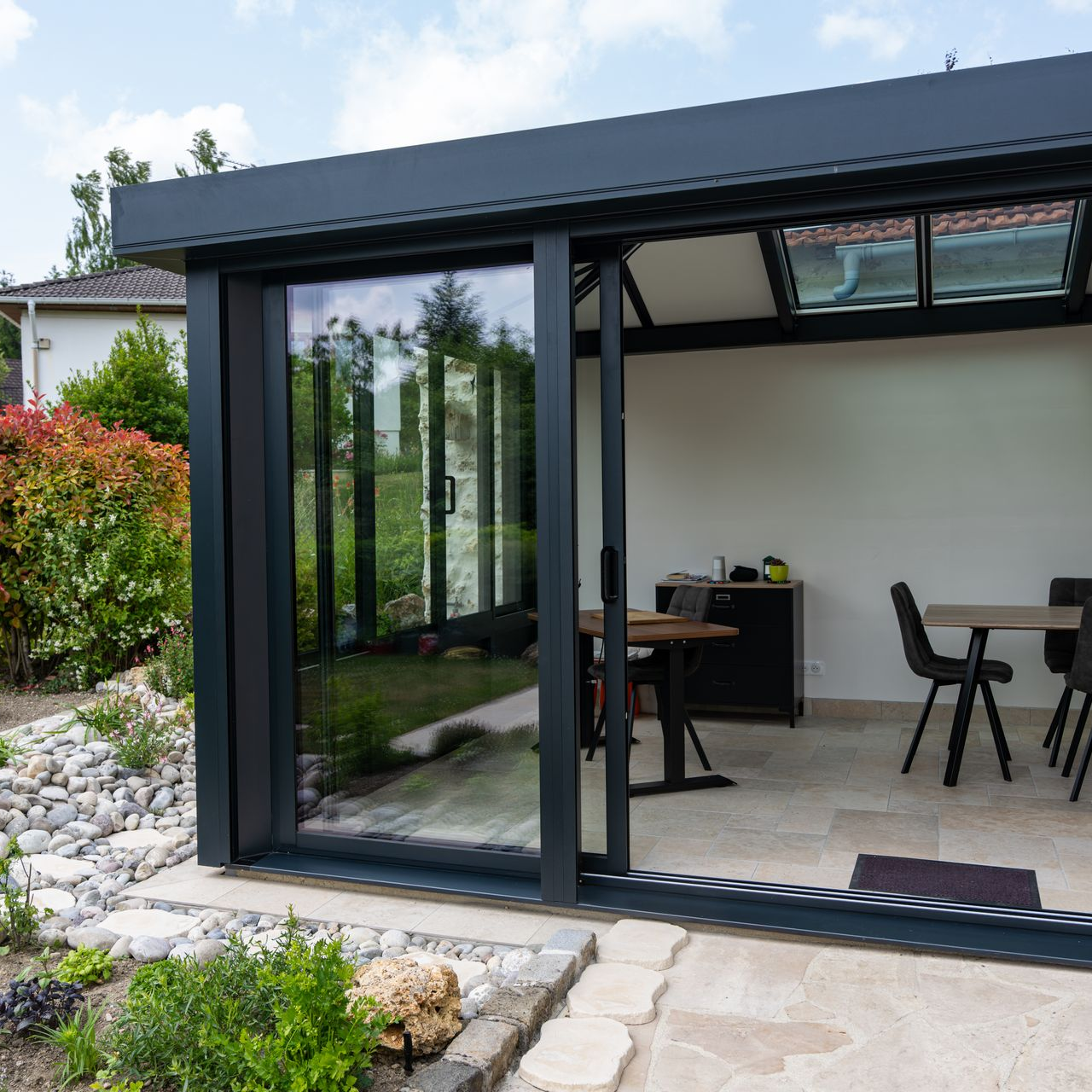 Véranda moderne noire en aluminium, avec des portes vitrées coulissantes.
