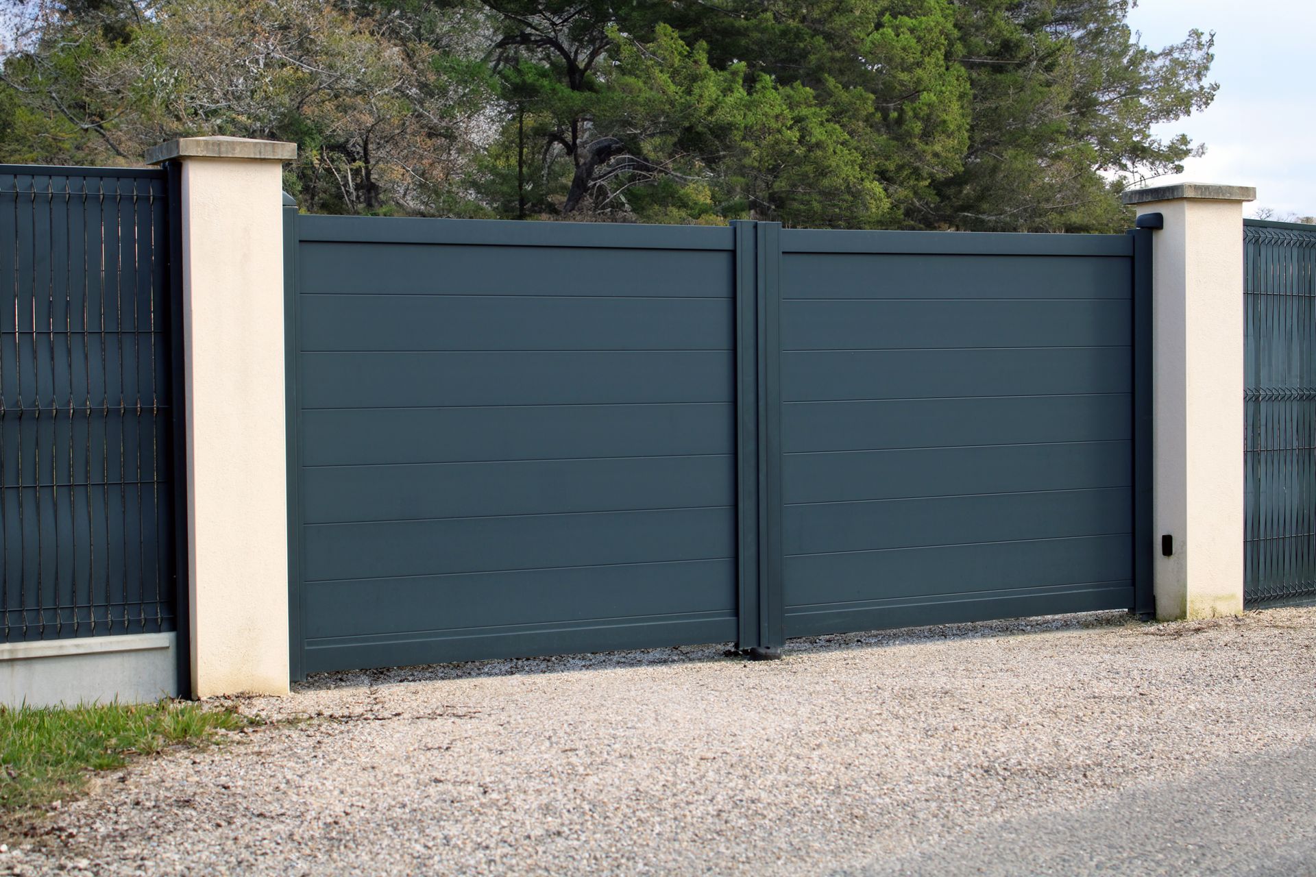 Portail battant en aluminium gris avec piliers en maçonnerie.