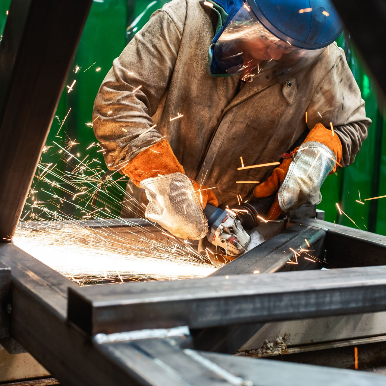 Un soudeur fait du meulage sur une pièce métallique en atelier industriel.