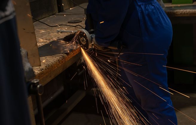 Un ouvrier découpe une pièce métallique. Des nombreuses étincelles sont produites.