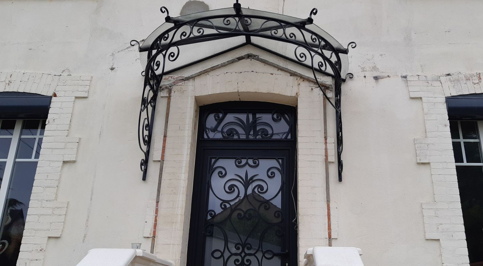 Marquise en fer forgé au-dessus d'une porte d'entrée métallique décorative.
