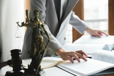 Una persona vestida de traje revisa documentos en un escritorio con una estatua de la Dama de la Justicia y un mazo.