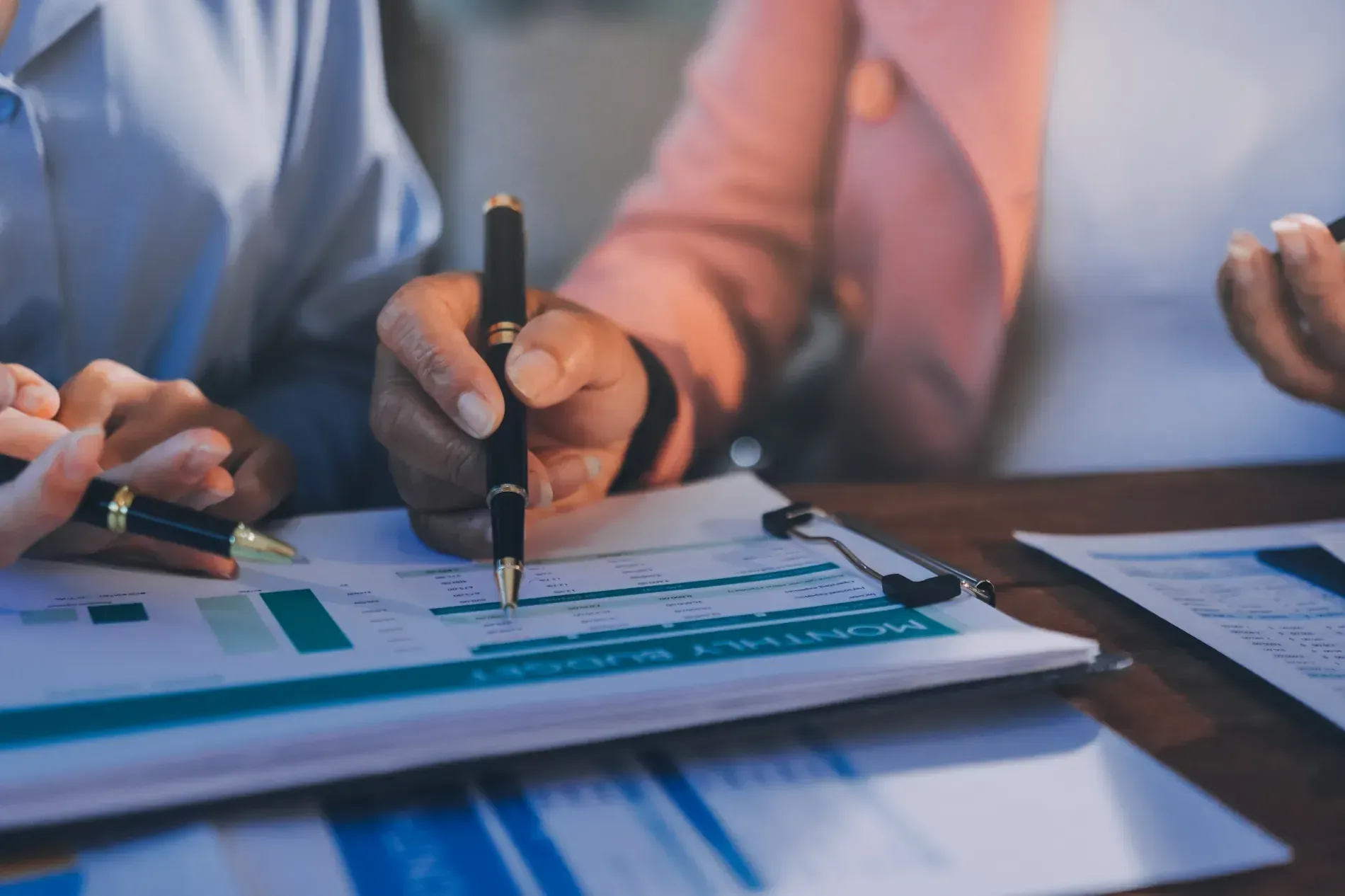 Manos sosteniendo bolígrafos, revisando informes financieros sobre un escritorio.