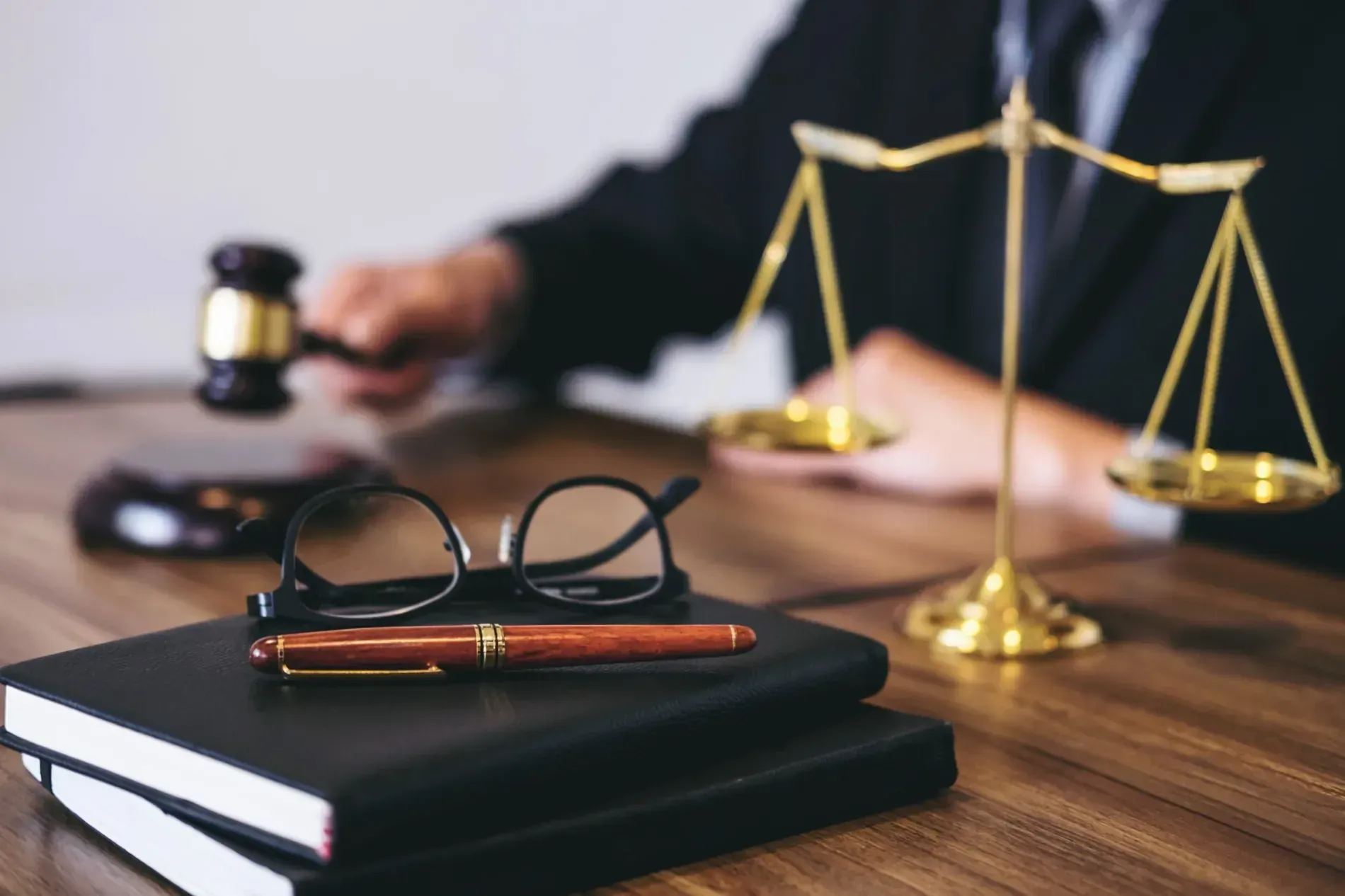 En una oficina, una persona habla con un cliente mientras un mazo y una balanza de la justicia reposan sobre una mesa.