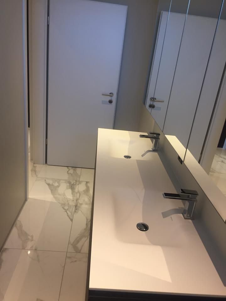 Salle de bains moderne avec meuble-lavabo blanc, miroir et sol carrelé, vue sur une porte fermée.