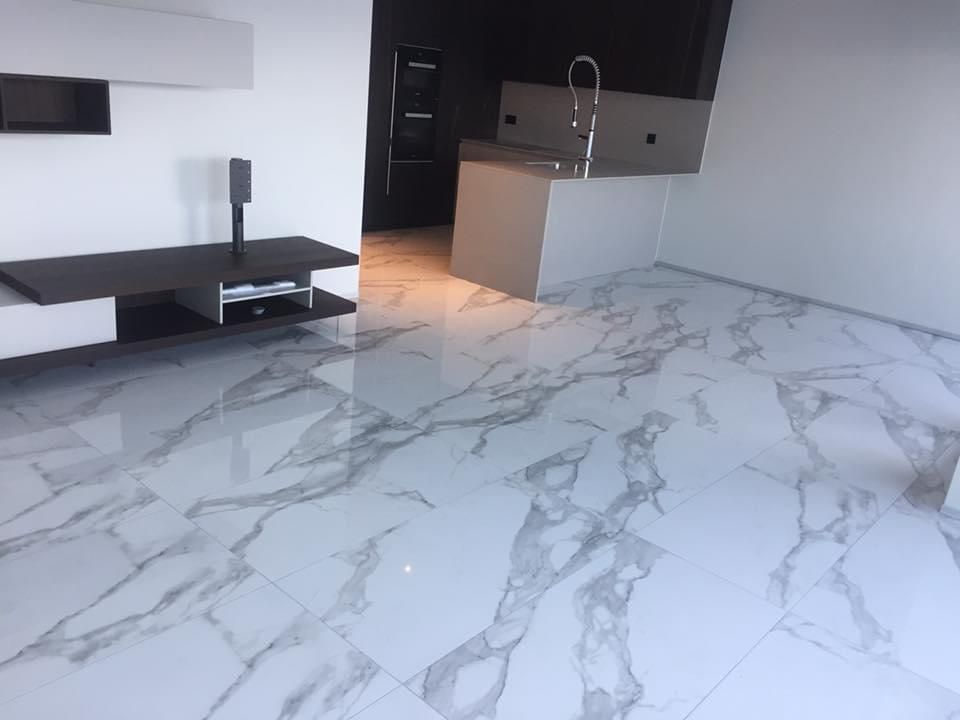 Salon moderne avec sol en carrelage de marbre brillant, meuble TV noir et îlot de cuisine blanc.