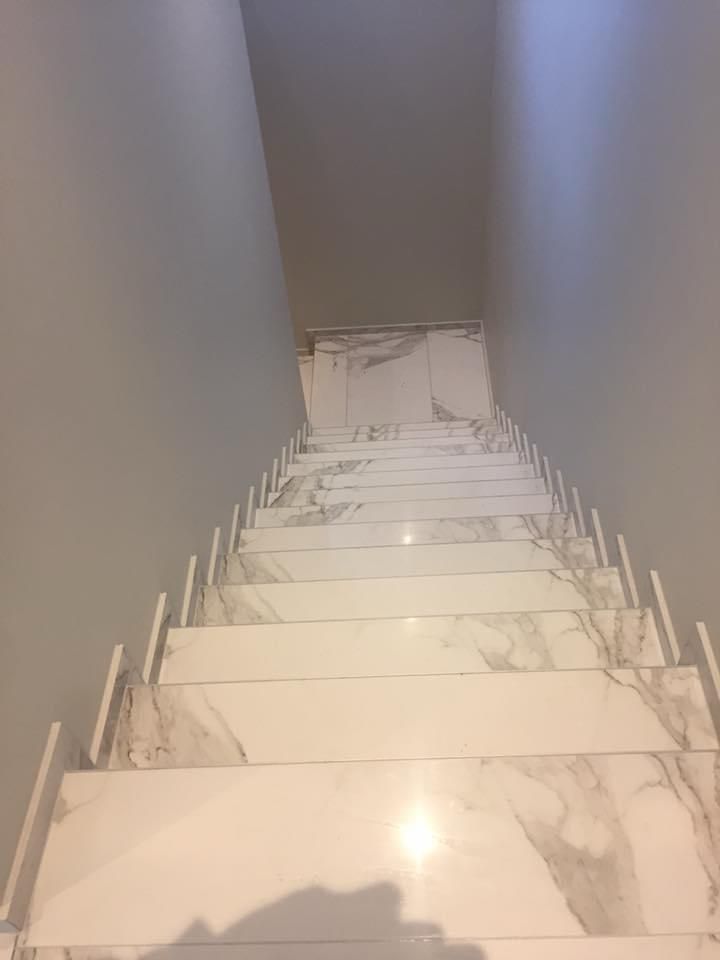 Escalier en marbre vu d'en bas, avec des murs gris et un palier à l'éclairage tamisé au-dessus.