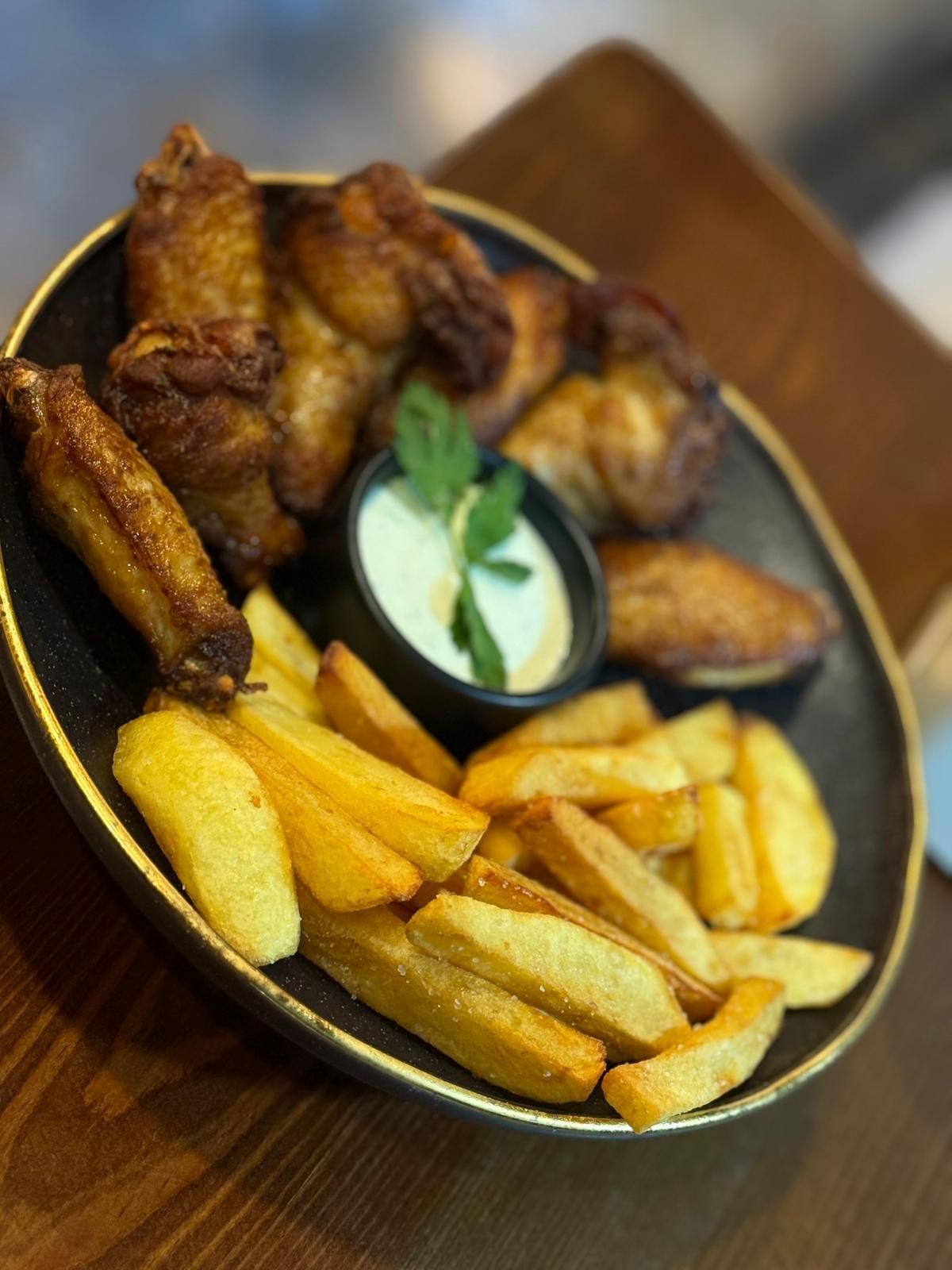 Un plato de alitas de pollo y patatas fritas en una mesa de madera.