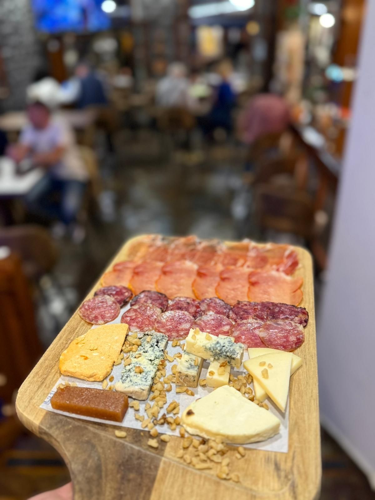 Una persona sostiene una tabla de cortar de madera con carne y queso encima.