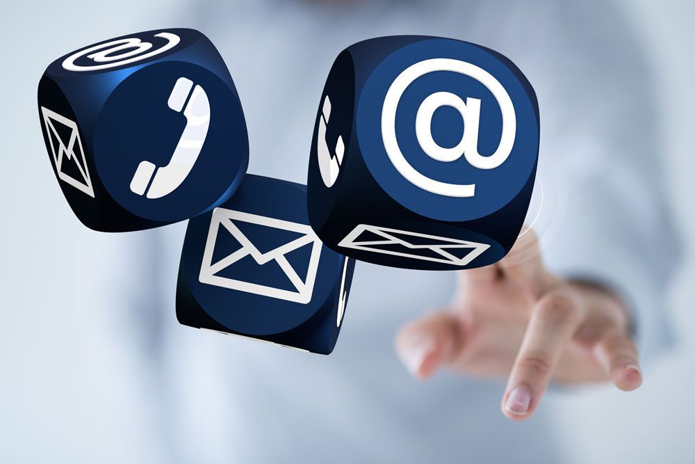 Eine Hand hält einen Würfel mit einer Telefon-E-Mail und einem @ darauf
