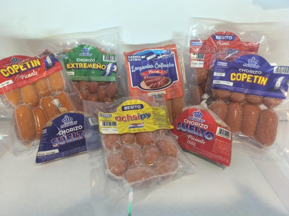 Paquetes de varias salchichas con etiquetas de colores sobre una superficie blanca.