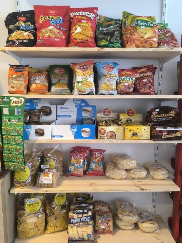 Estantes repletos de diversos snacks envasados, incluidas patatas fritas, galletas y pan en un entorno de tienda.