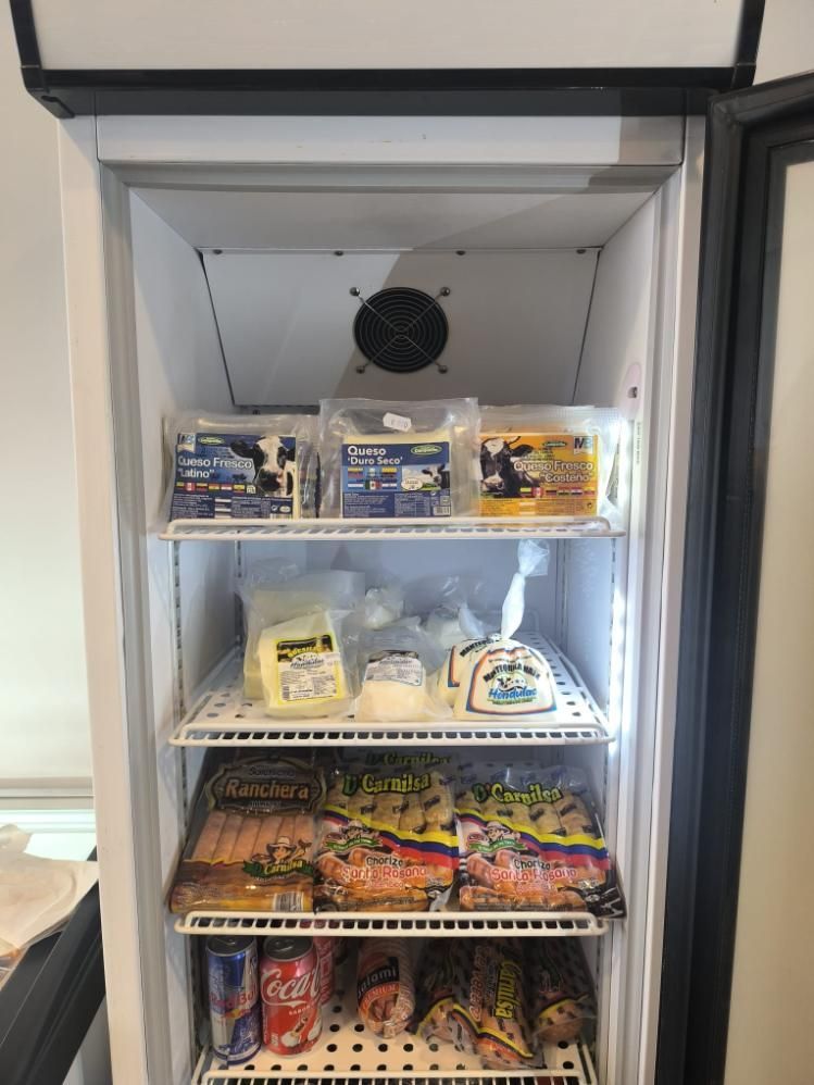 Refrigerador lleno de queso, bebidas y otros alimentos en estantes de alambre.
