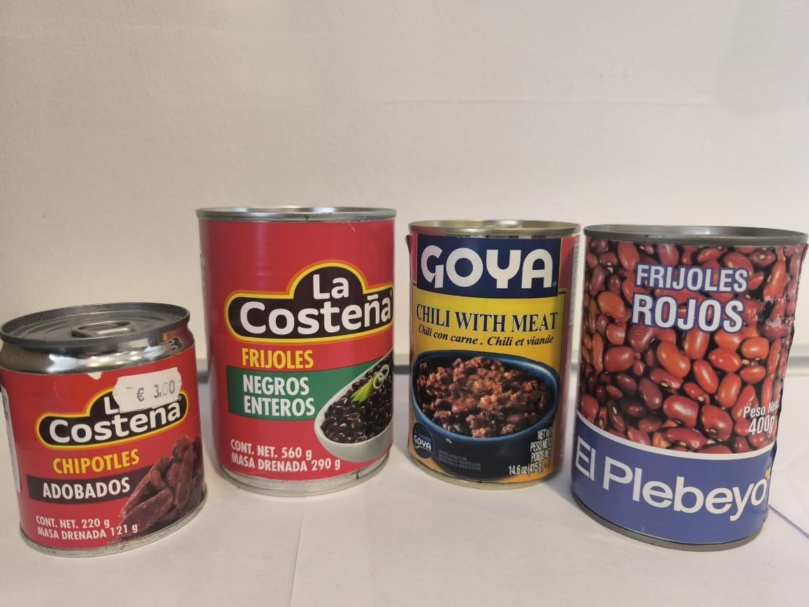 Cuatro latas de frijoles de diferentes marcas, incluidos frijoles negros, chipotle y rojos.