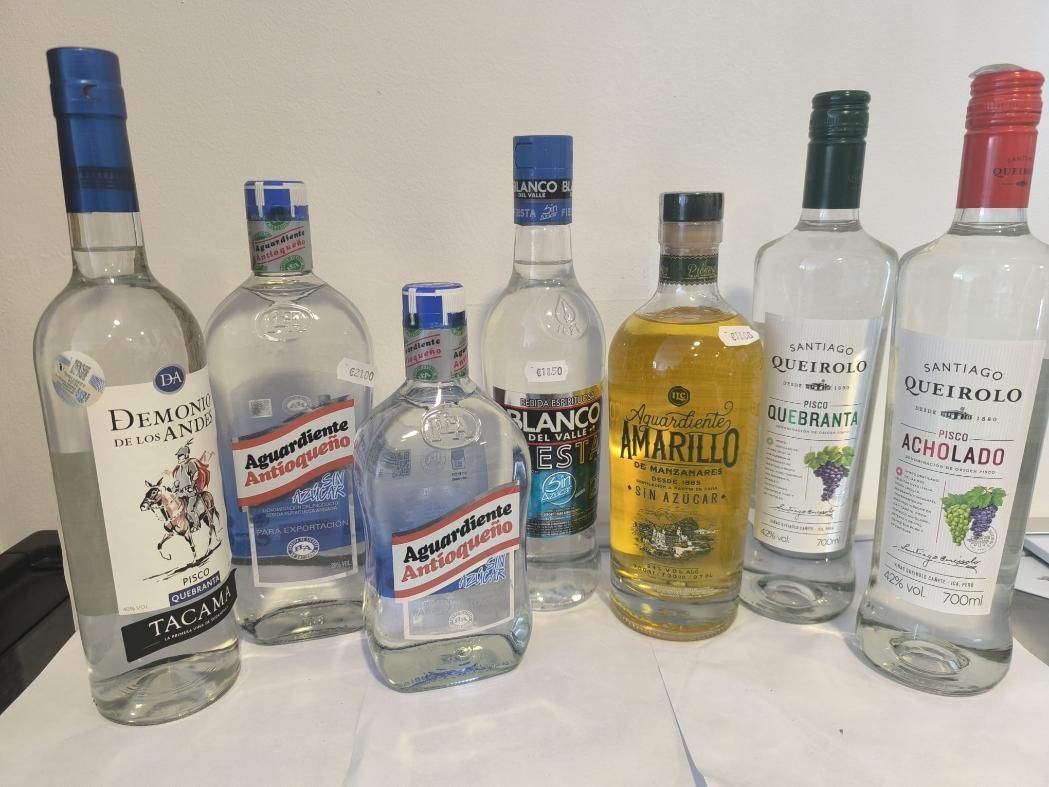 Botellas de licor, en su mayoría de vidrio transparente, con etiquetas y tapas de colores, sobre una mesa.