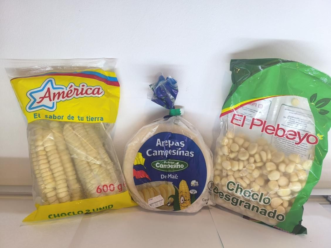 Tres bolsas de productos de maíz: mazorcas de maíz, arepas y maíz desgranado, sobre un fondo blanco.