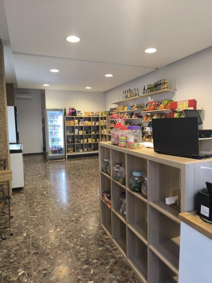 Dentro de una tienda: estantes con productos envasados, una vitrina refrigerada y un mostrador con un portátil y frascos.