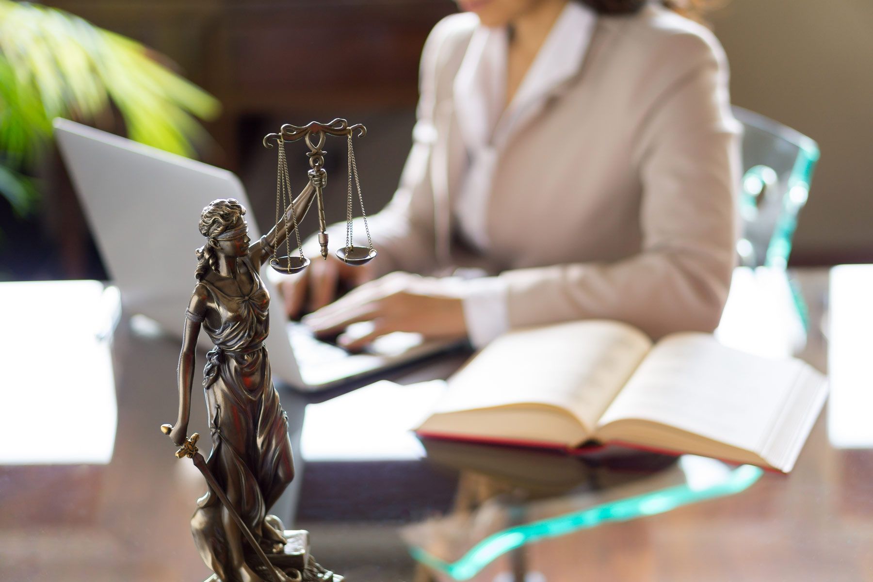 Une avocate tapant sur le clavier de son ordinateur avec une statuette de Thémis, symbole de la justice, au premier plan