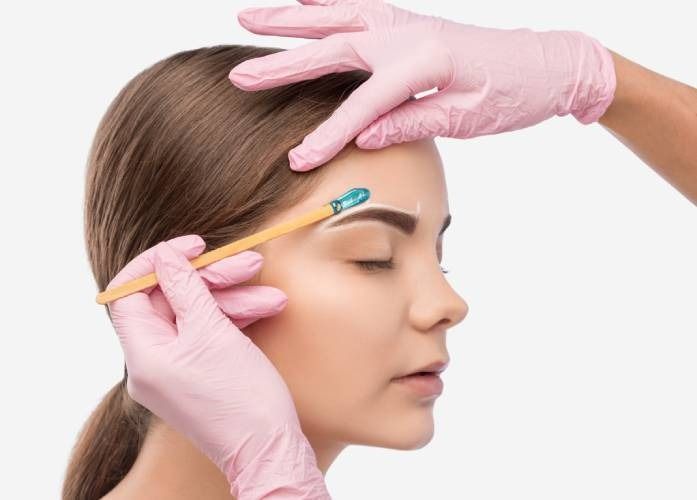Una mujer se pinta las cejas con una mujer que lleva guantes rosas.