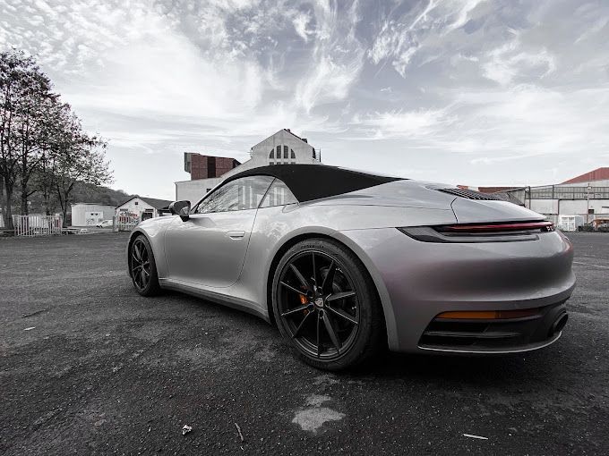 Auf einem Parkplatz steht ein silbernes Porsche 911 Carrera Cabrio.