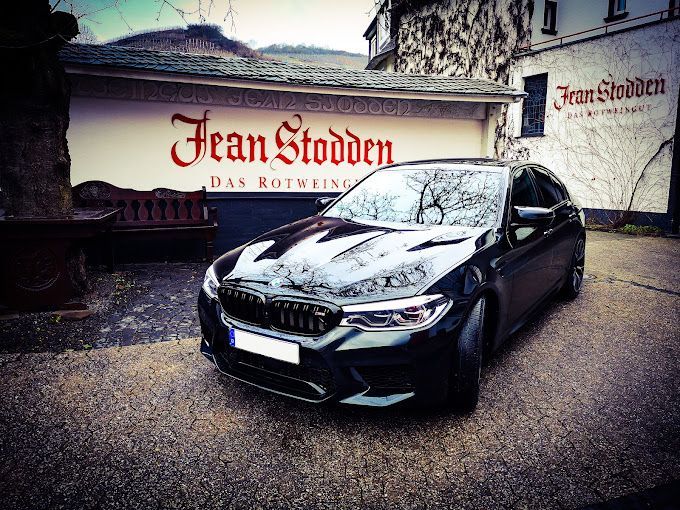 Ein schwarzes Auto steht vor einem Gebäude mit der Aufschrift „Jean Stoden“