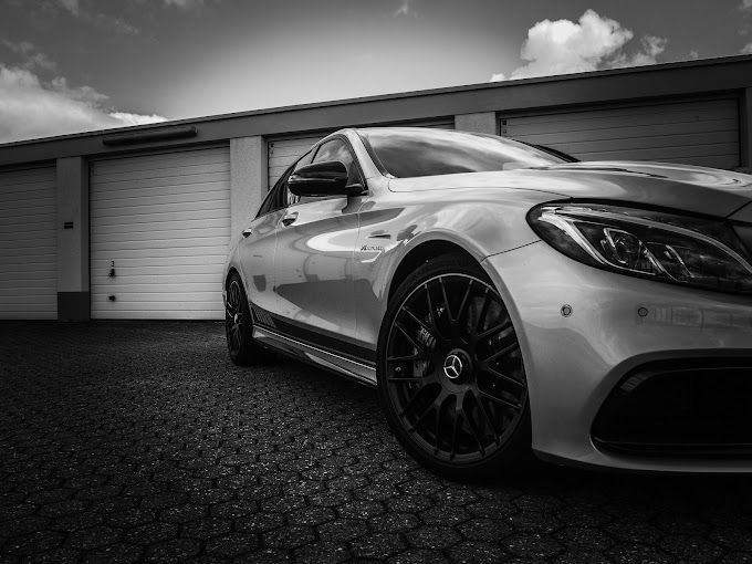 Ein Schwarzweißfoto eines silbernen Autos, das vor einer Garage geparkt ist.