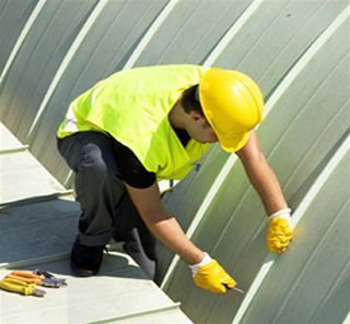 Un hombre que lleva un casco amarillo está trabajando en un tejado.