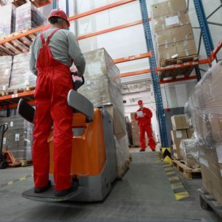Un hombre con un mono rojo conduce una carretilla elevadora en un almacén.