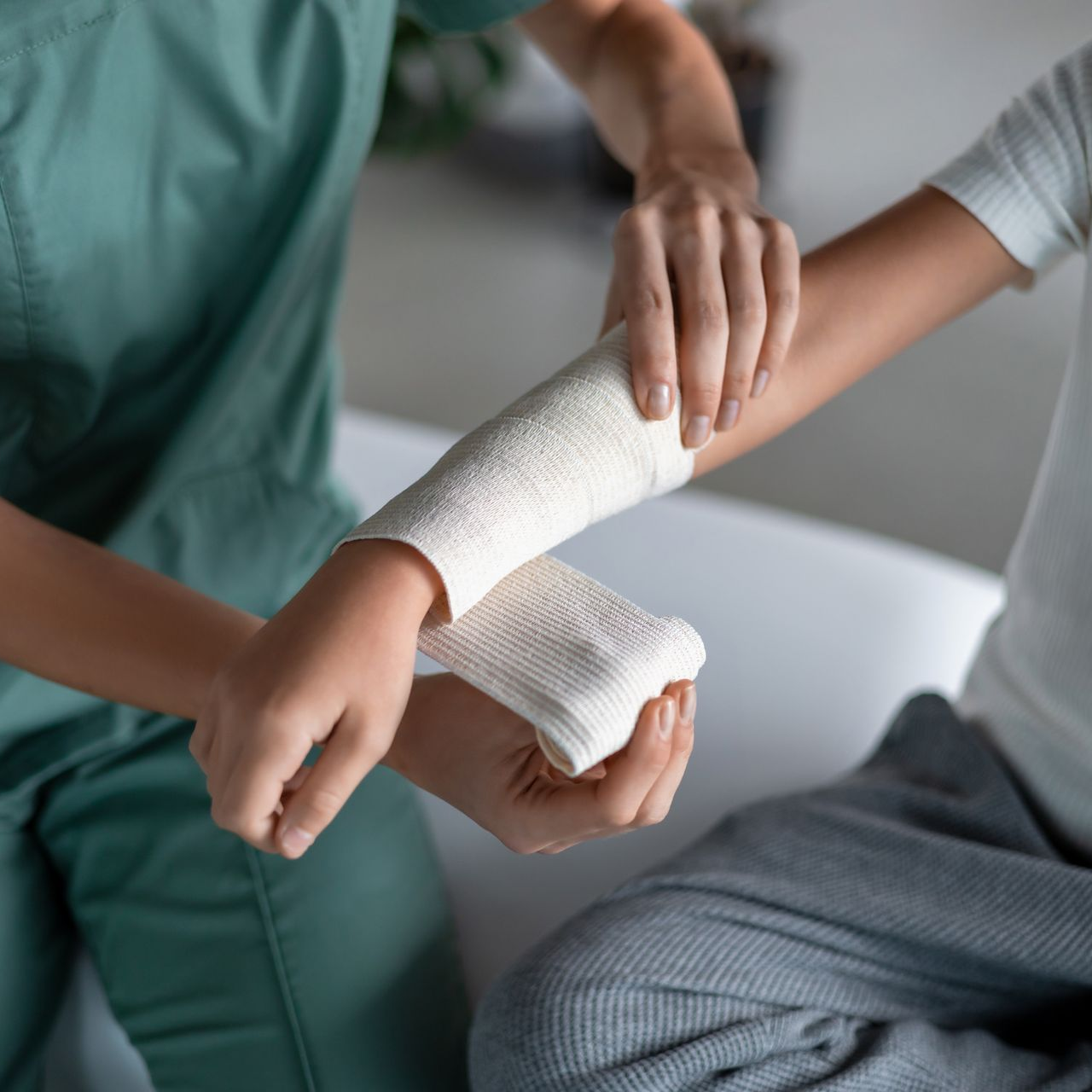 Des mains enroulant un bandage blanc autour d'un poignet dans une clinique