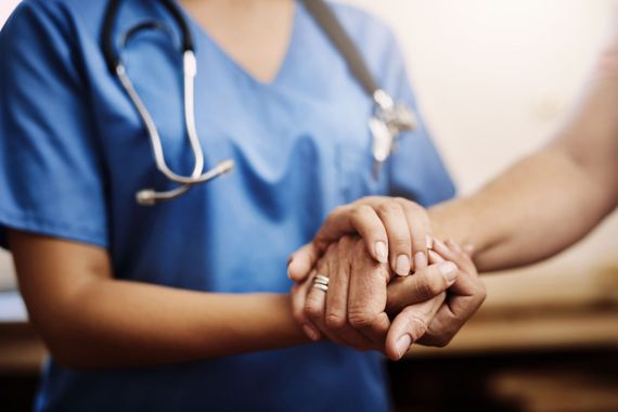 Une infirmière en blouse bleue tient les mains d'un patient dans un environnement hospitalier bienveillant.