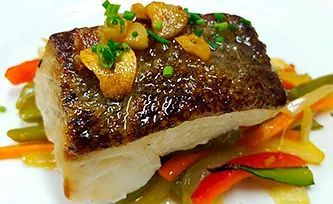 Un plato blanco cubierto con un trozo de pescado y verduras.