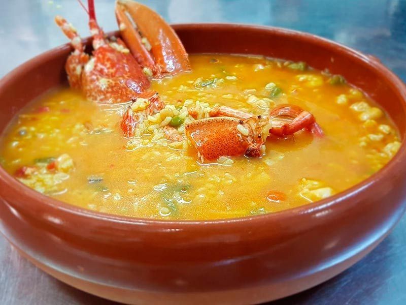 Un tazón de sopa con arroz y langosta en una mesa.