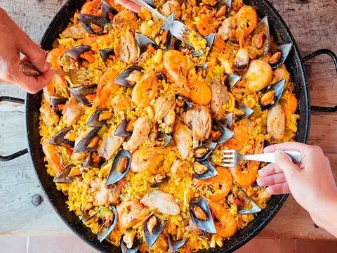 Una persona sostiene un tenedor sobre una sartén de paella.
