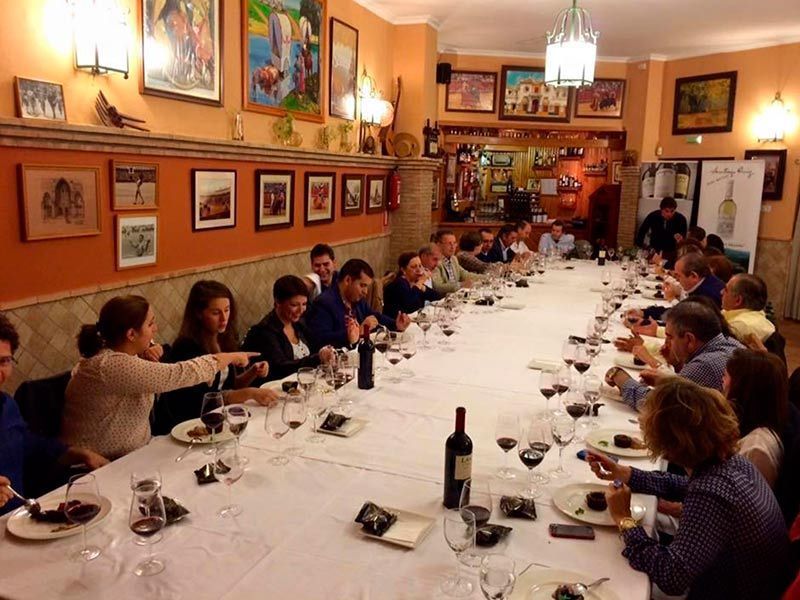 Un grupo de personas está sentado en una mesa larga con copas de vino.