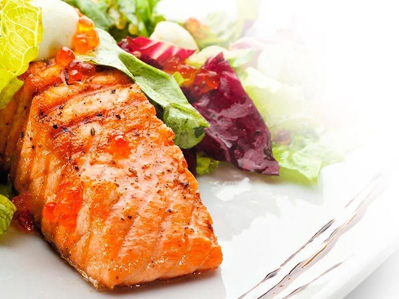 Un plato blanco cubierto con un trozo de salmón y una ensalada.