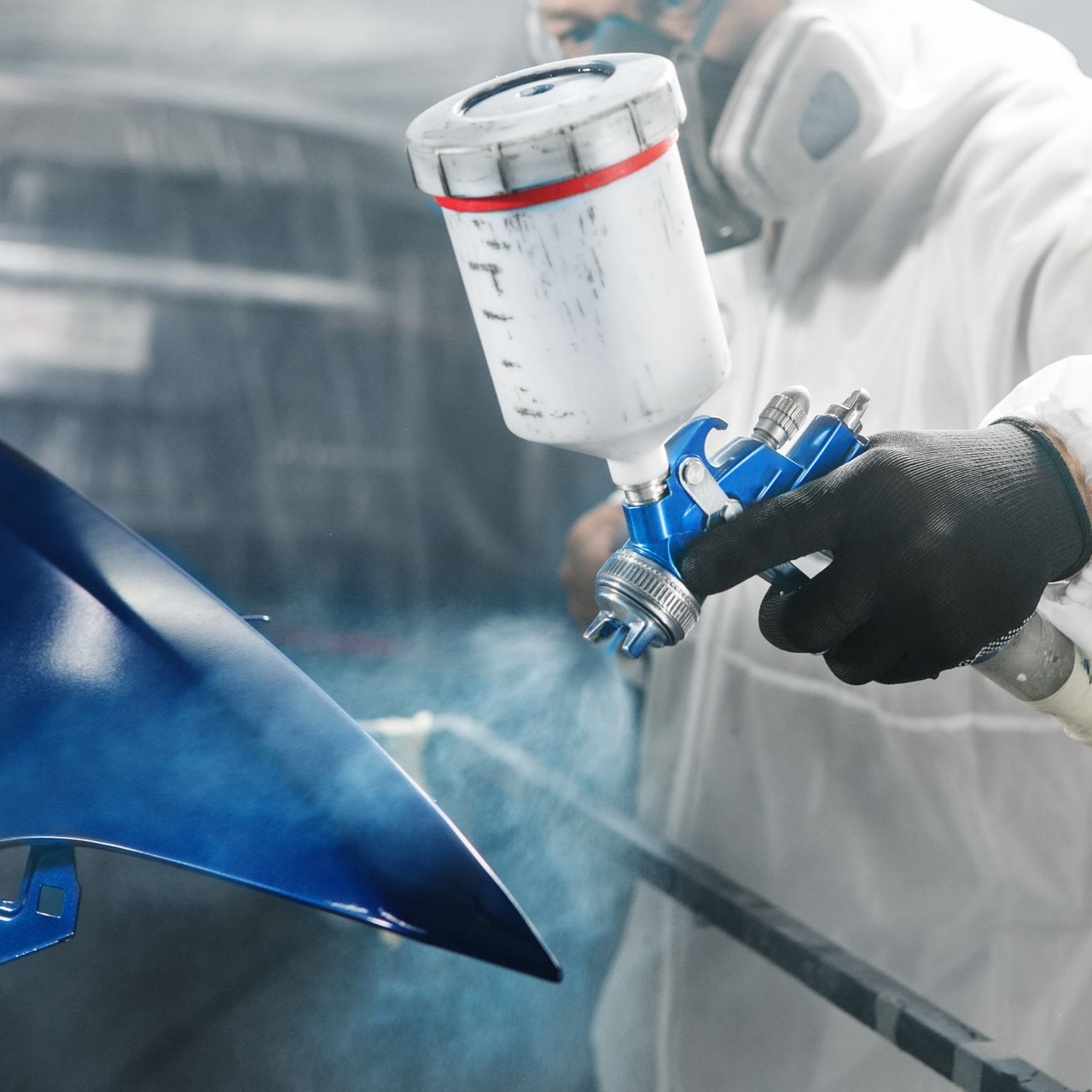 Une personne pulvérise de la peinture bleue sur un objet dans un atelier