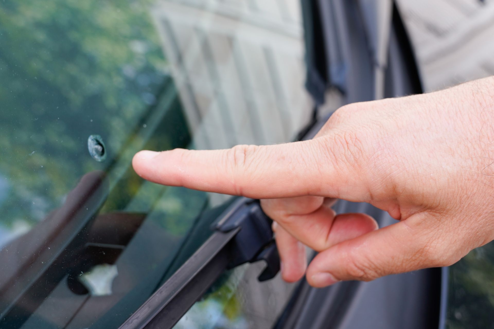 Pointage du doigt d'une fissure sur le pare-brise d'une voiture, à l'extérieur