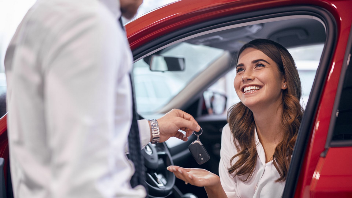 Un vendeur de voitures remet des clés de voiture à une femme souriante dans une voiture rouge