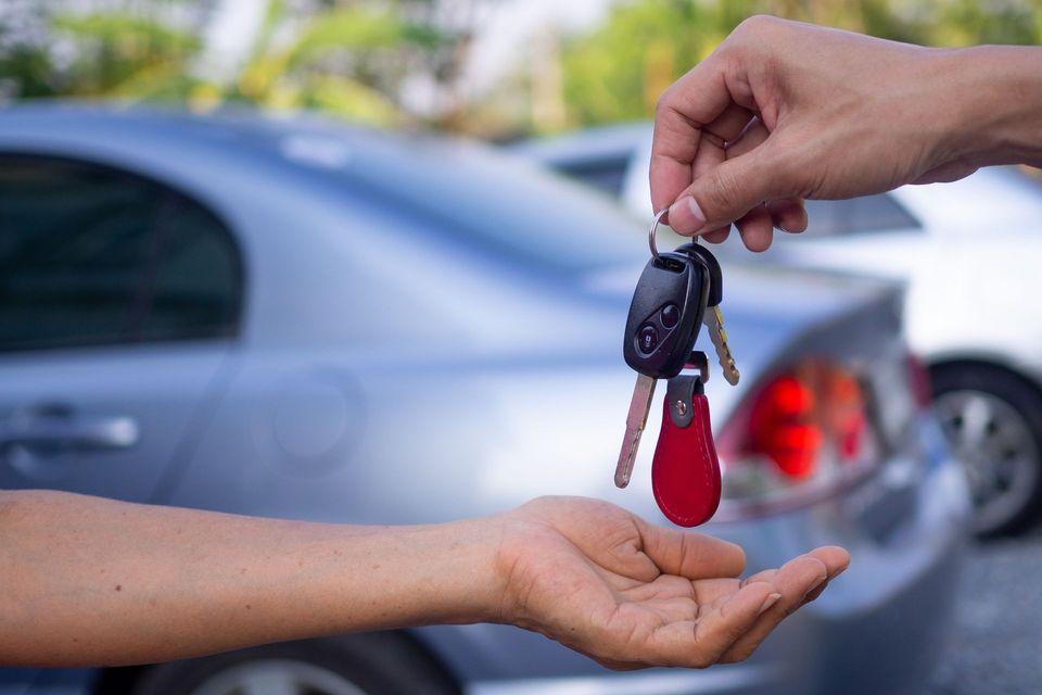 Une personne remet des clés de voiture à une autre personne devant une voiture