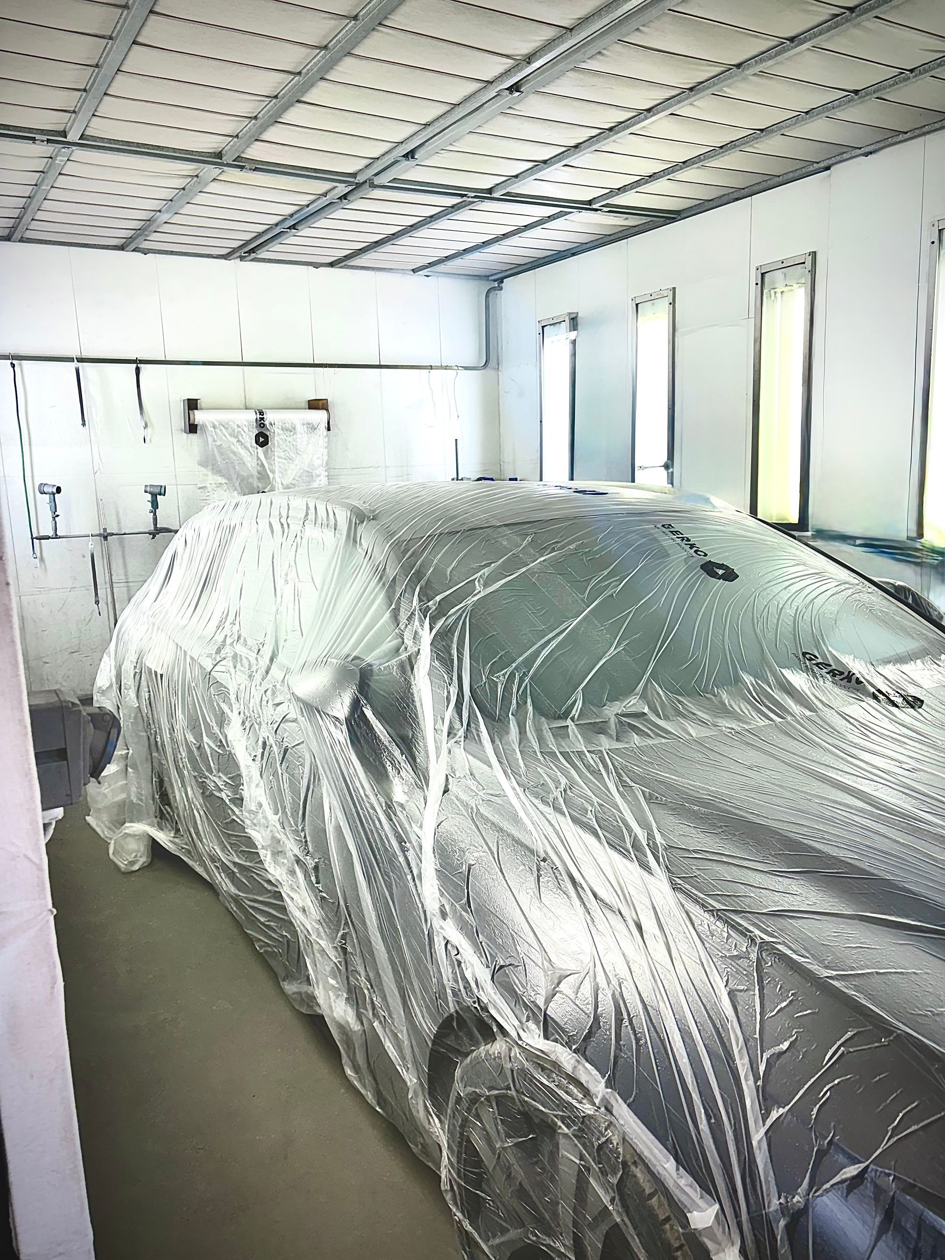 Une personne pulvérise de la peinture sur une voiture dans une cabine de peinture