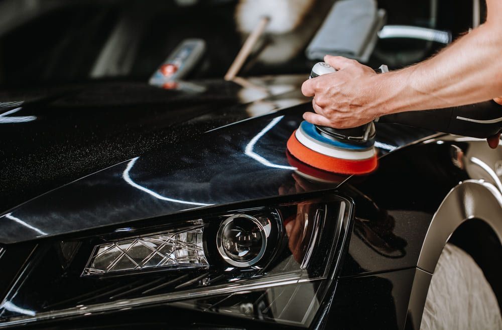 Ein Mann poliert ein schwarzes Auto mit einer Bürste | Gotthelf Garage AG