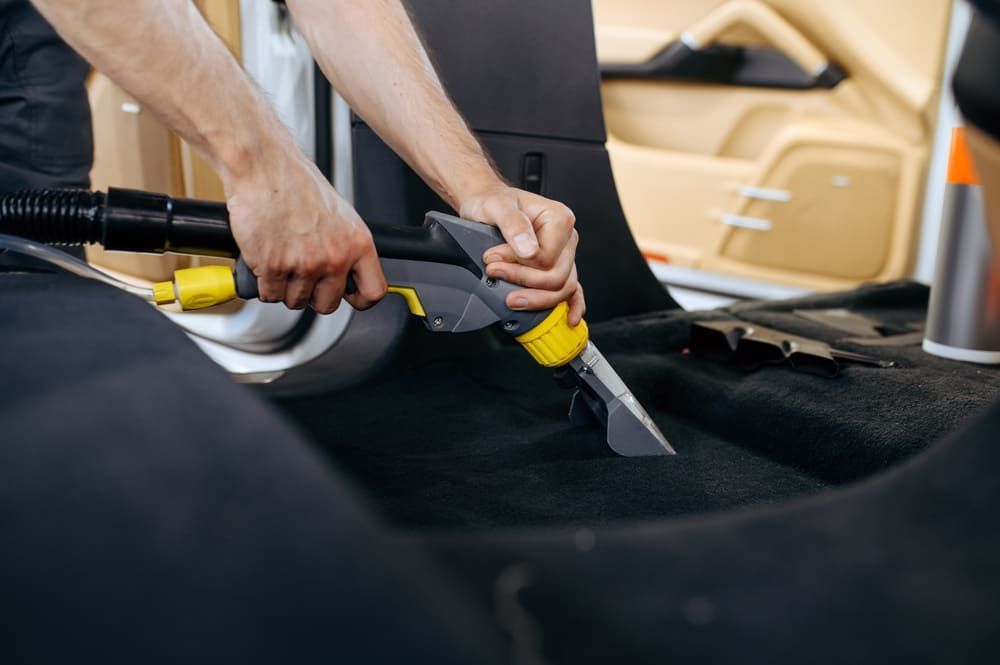 Ein Mann reinigt den Boden eines Autos mit einem Staubsauger | Gotthelf Garage AG
