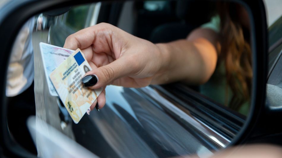 Mano sosteniendo una licencia de conducir y otro documento de identidad, probablemente en la ventanilla de un coche.