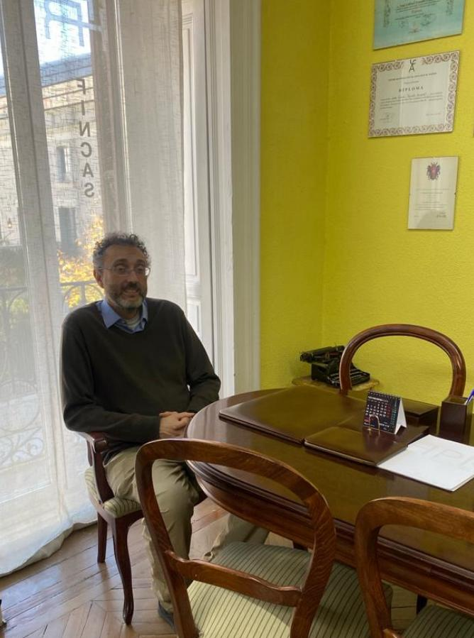 Hombre sentado en un escritorio en una oficina. Pared amarilla, ventana y certificados.