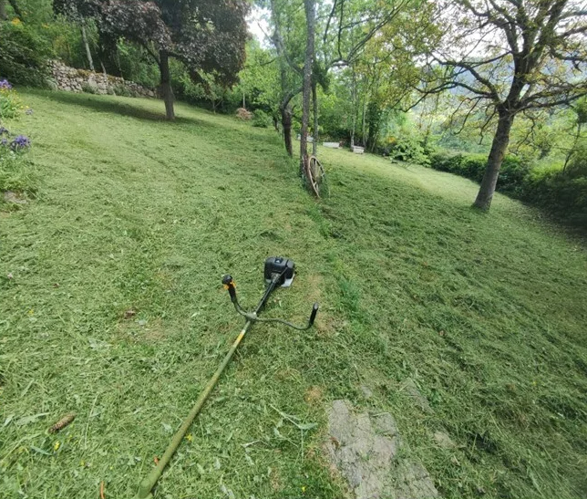 Une débroussailleuse est posée sur une colline herbeuse fraîchement tondue.