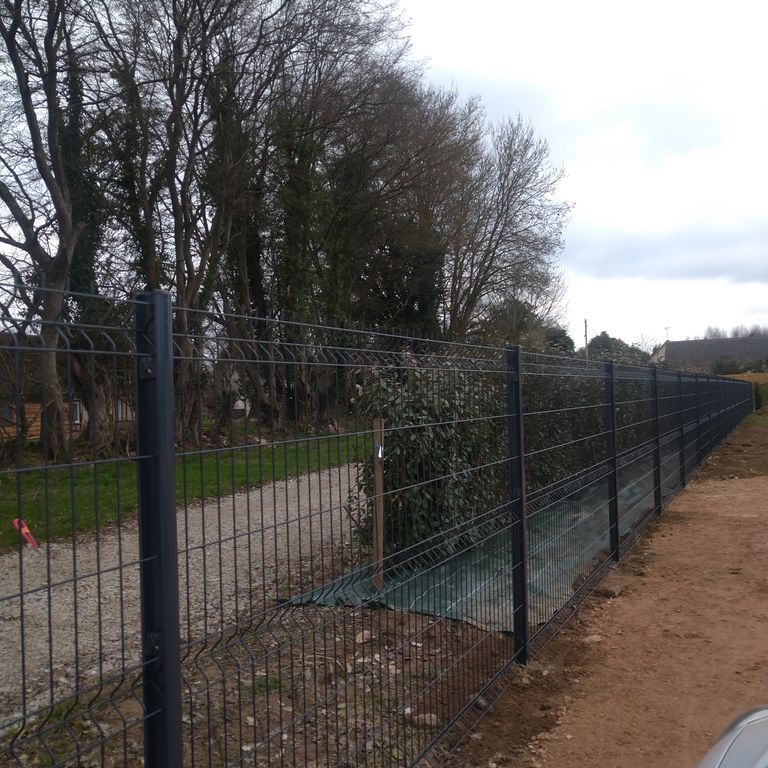Une clôture en grillage gris foncé longe un chemin de gravier.