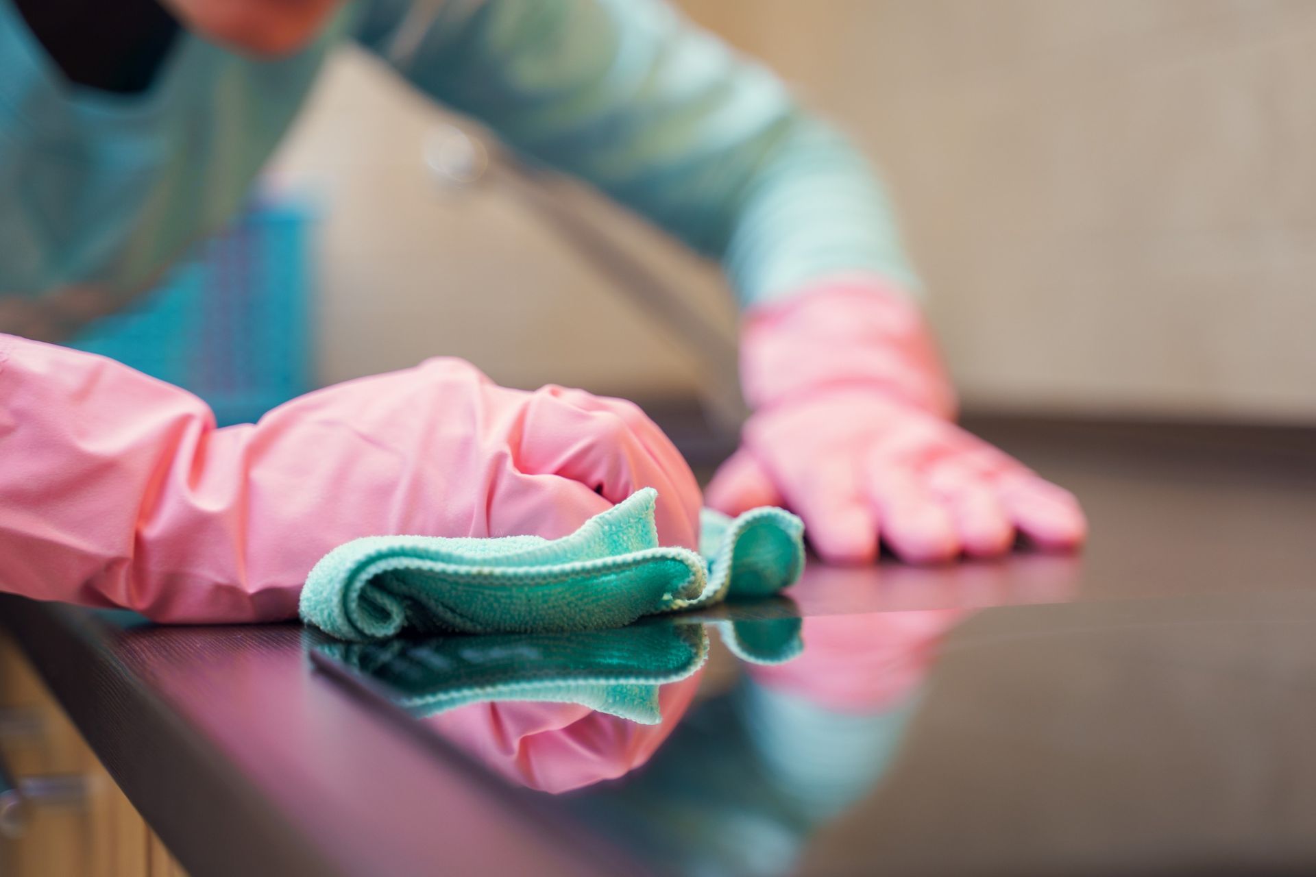 Una mujer que lleva guantes rosas está limpiando un mostrador con un paño.