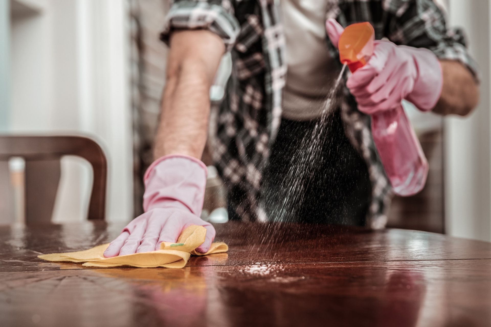 Un hombre está limpiando una mesa de madera con un paño y una botella de spray.