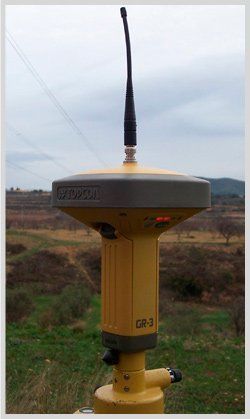 Un dispositivo amarillo y negro con una antena en la parte superior se encuentra en un campo.