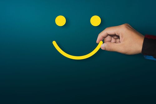 Une main dessine un smiley jaune sur un fond bleu sarcelle foncé.